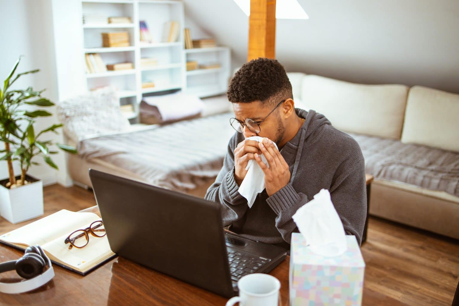 African-American man works at home blows his nose due to nasal obstruction.