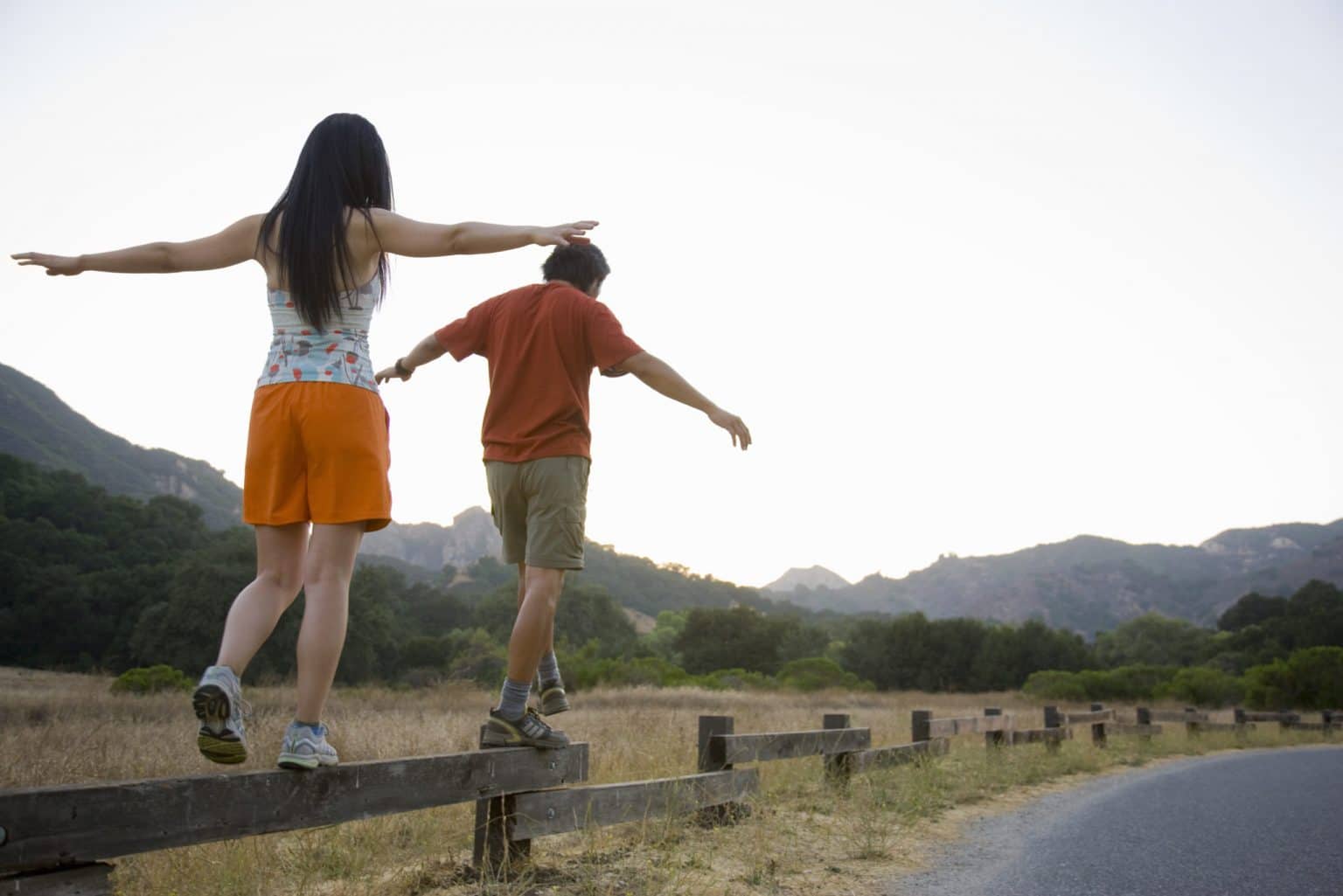 Two people walking on a short fence with their arms out while balancing and not facing the camera
