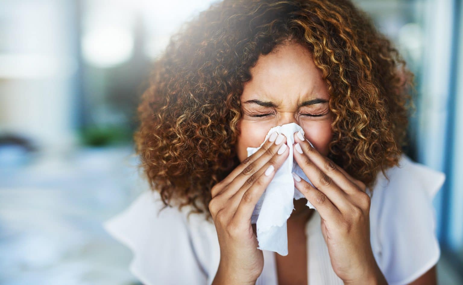 Shot of a woman using a tissue to sneeze in while experiencing post nasal drip.