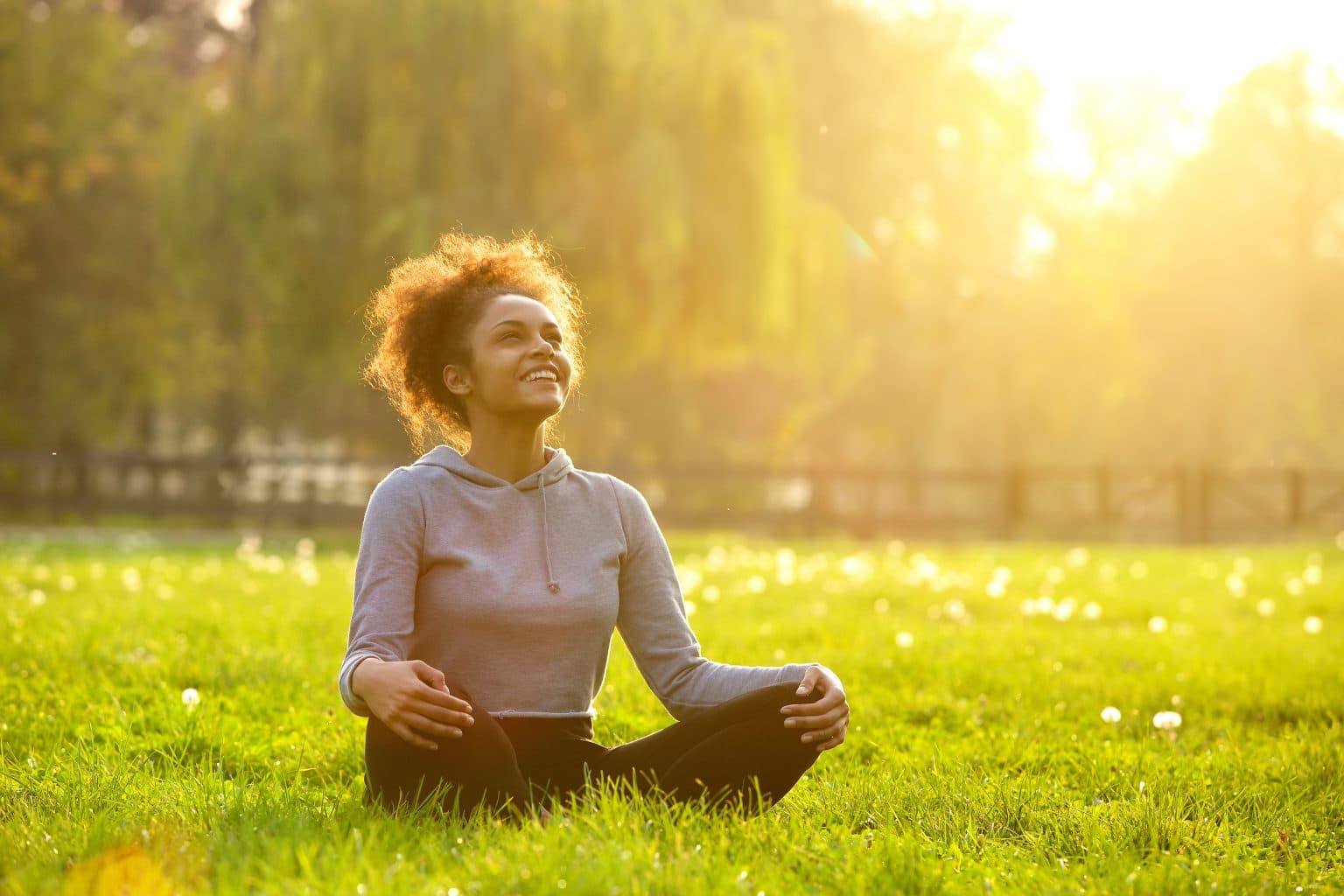 Young woman sitting outdoors in yoga position while breathing clearly after nasal polyp procedure.