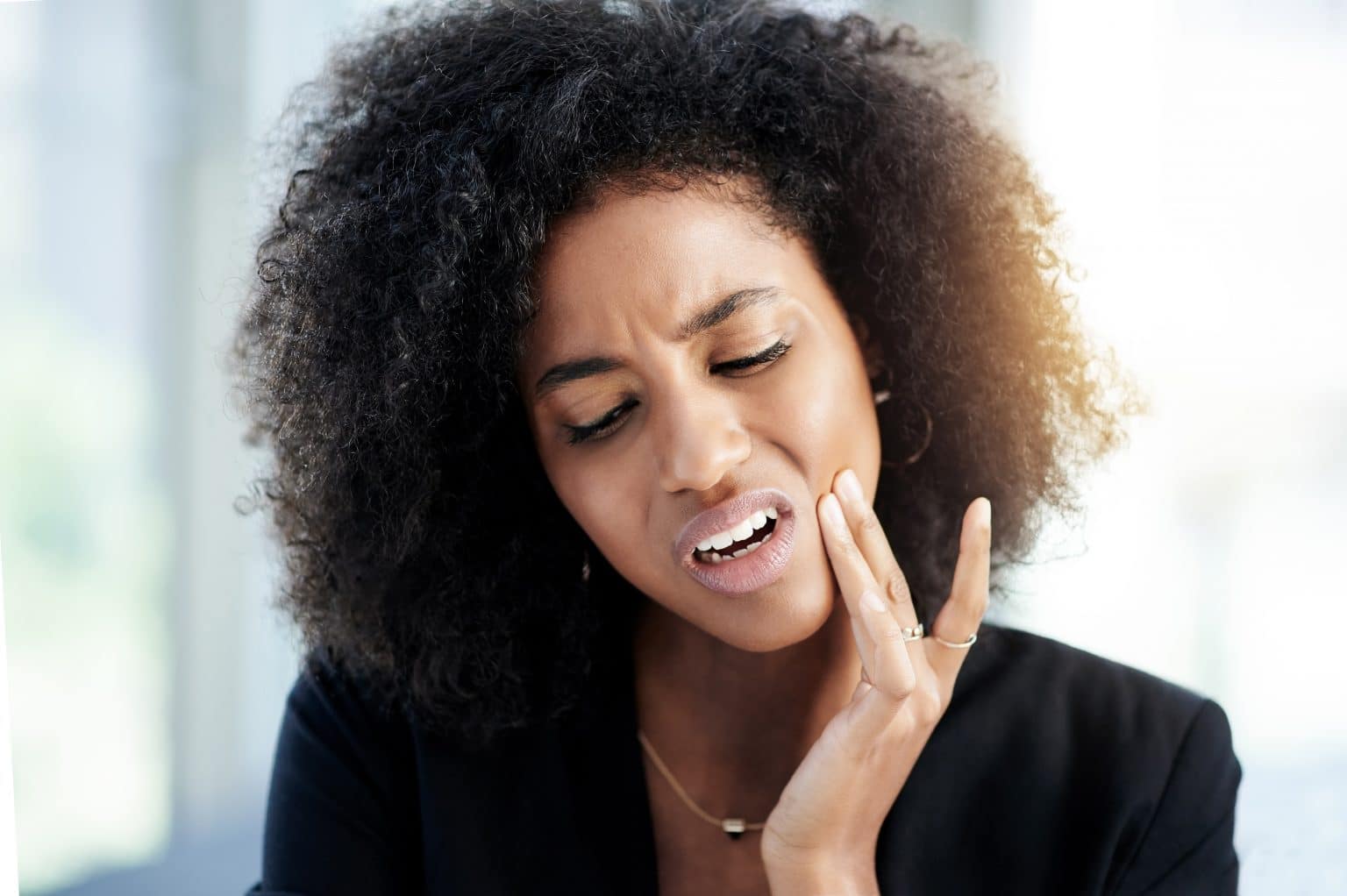 Woman holds her hand up to her jaw in pain from her TMJ symptoms